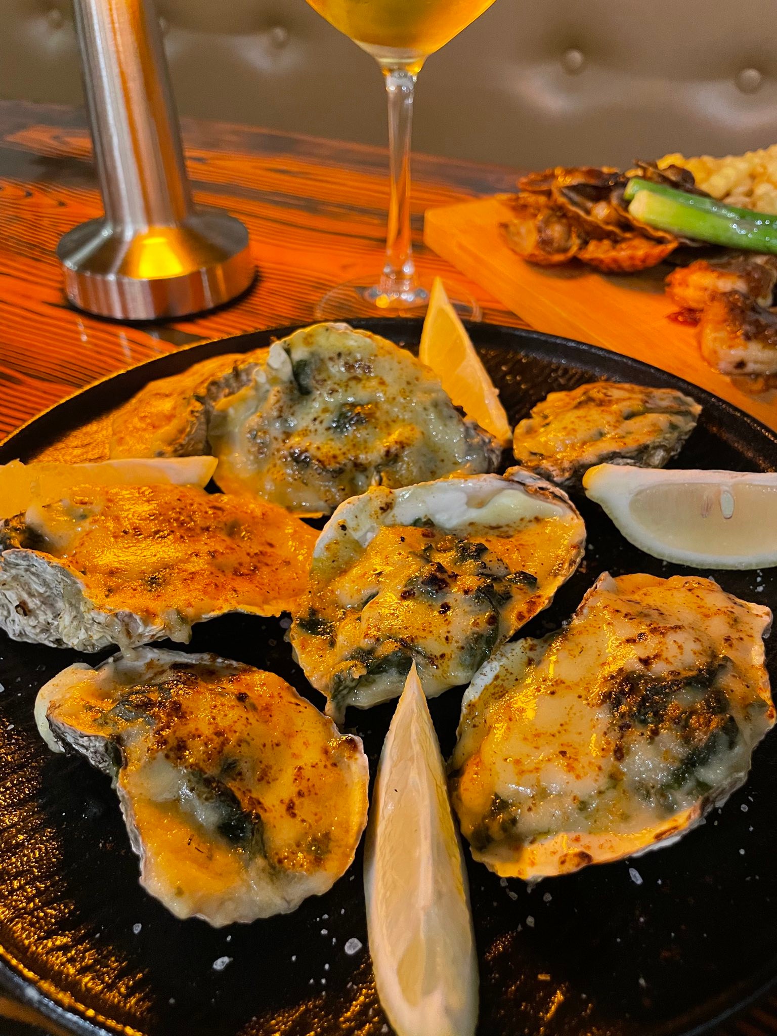 Baked oysters on cast iron skillet with lemon wedges — fresh seafood at Lola's